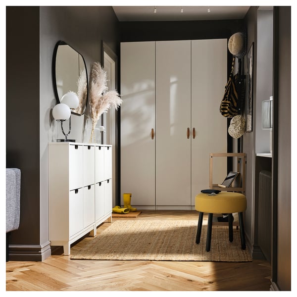 Modern entryway with white cabinets, a round yellow stool, and a jute rug on wooden floors.