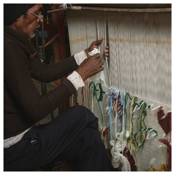 Person weaving rug. Brown sweater, jeans. Threads around loom.