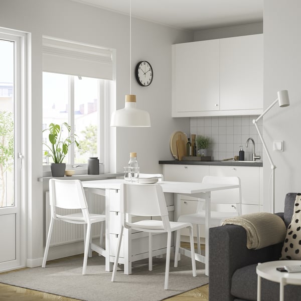Modern kitchen with NORDEN table & stackable chairs. Table has drawers, near window with pendant lamp. White cabinets, grey countertop & rug.