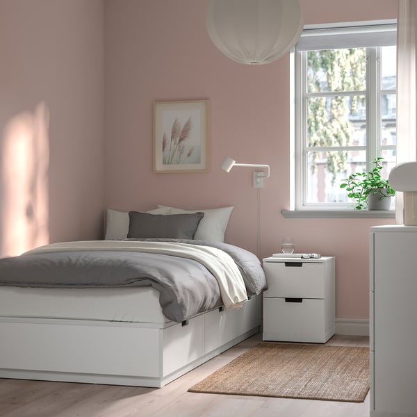 Minimalist bedroom with white bed, grey bedding, pink walls, window, & lamp.