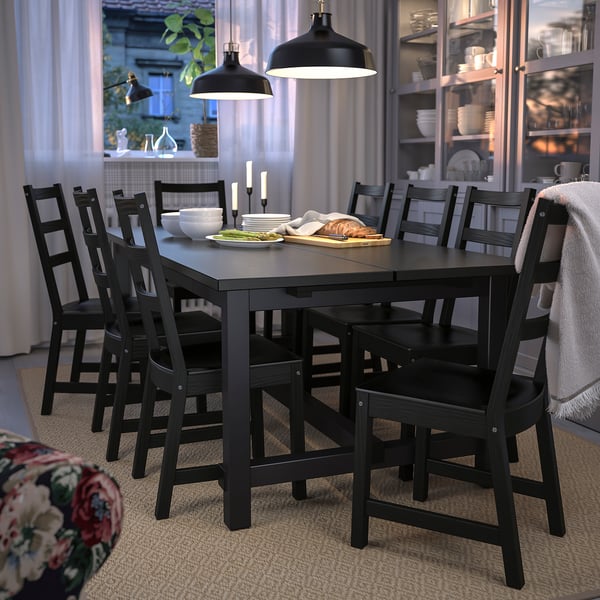 Modern black dining set with extendable table and ladderback chairs. Soft pendant lighting, dishware in glass cabinet.