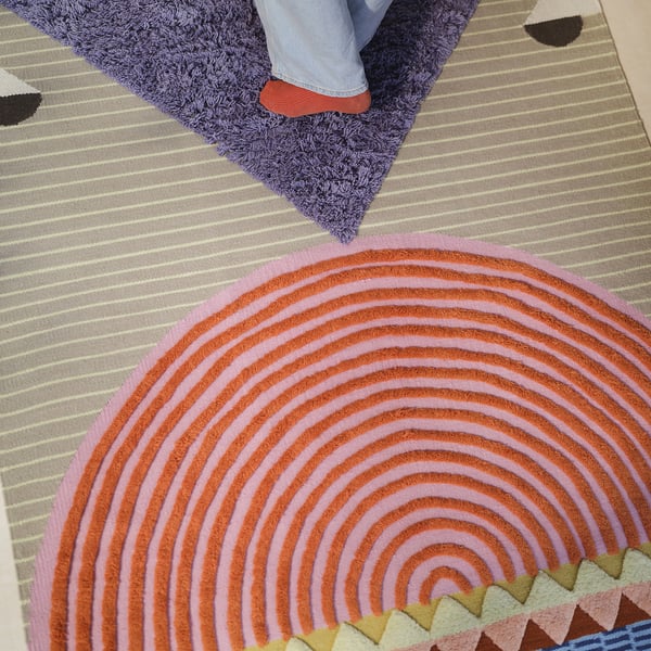 Handwoven rug with spiral pink & orange hues, diverse pile lengths, modern touch.