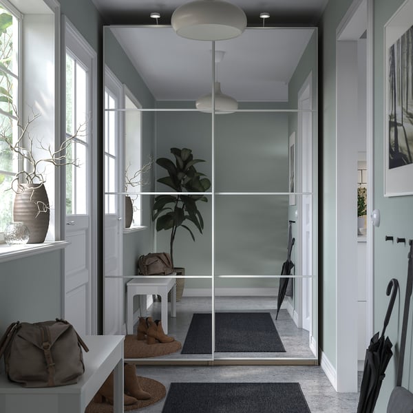 Modern entryway with PAX wardrobe, mirrored sliding doors, grey rugs, white walls, pendant lights, and potted plants.