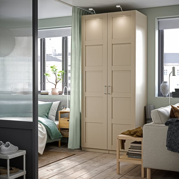 A modern room with beige PAX wardrobe, grey sofa, and green curtains, featuring a bed and balcony.