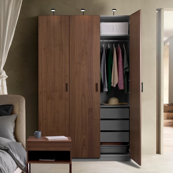Open wooden wardrobe revealing clothes, shelves, and drawers. Interior lighting highlights organised storage.