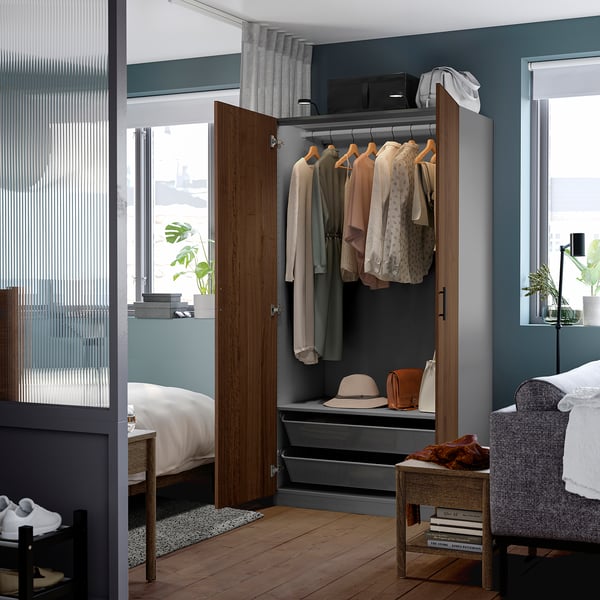 Modern bedroom with an open PAX wardrobe displaying clothes, hats, and accessories, featuring a full-length mirror and shelves.