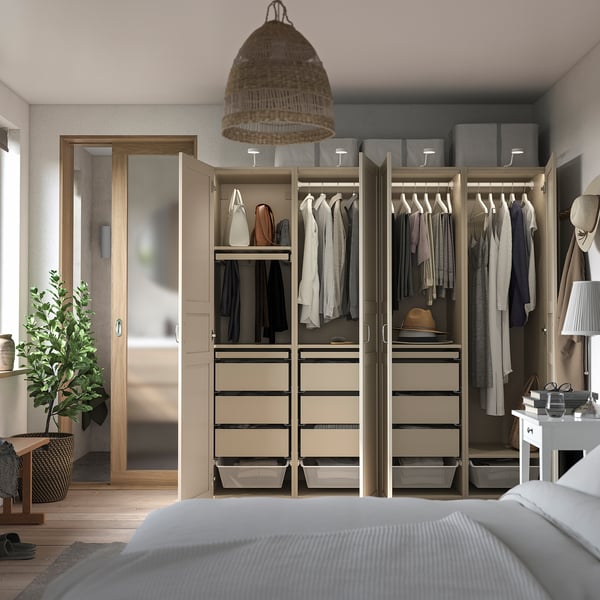 Modern walk-in closet with mirrored sliding doors, organised, beige drawers, hanging clothes, open wardrobe with storage boxes, and a large plant.
