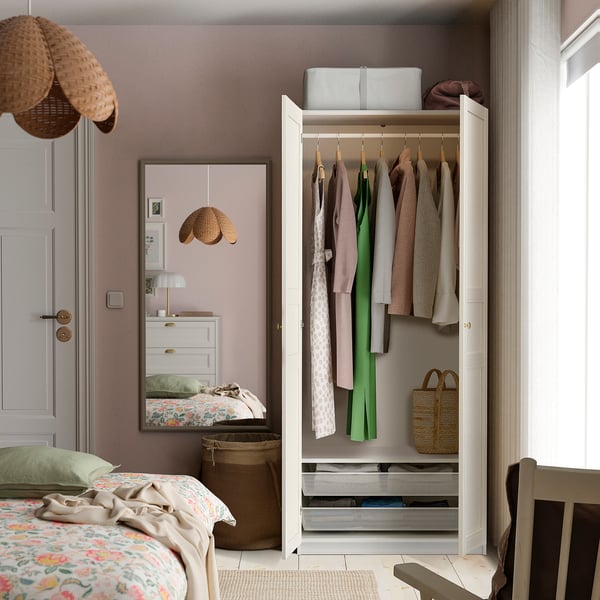 Bedroom with open wardrobe showing clothes, featuring PAX wardrobe by IKEA.