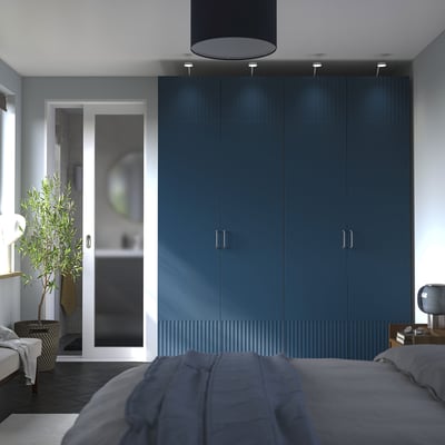Modern bedroom with blue PAX wardrobe, grey bed, wooden table, and glass door to bathroom with plant.