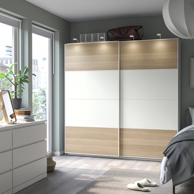 Modern bedroom with grey walls, light wood floor, PAX wardrobe, balcony view, grey bed, plant, and rug.