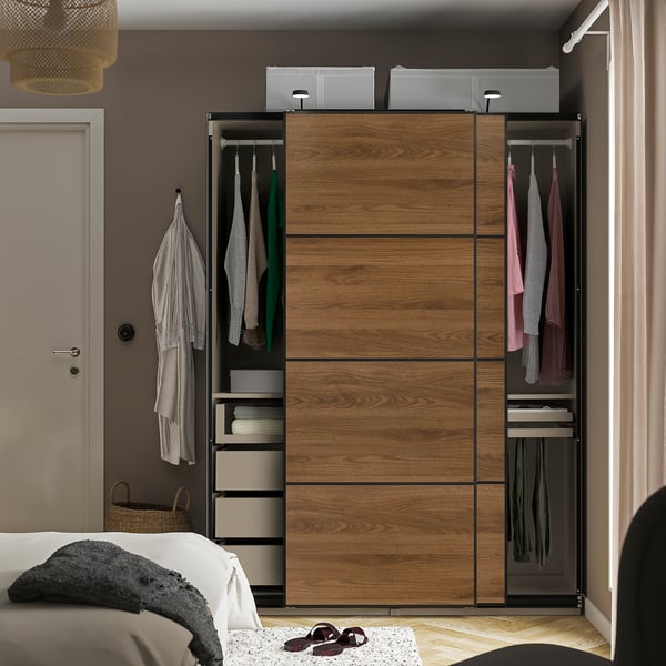 Modern bedroom with a wooden PAX wardrobe featuring sliding doors, hanging clothes, and shelves.