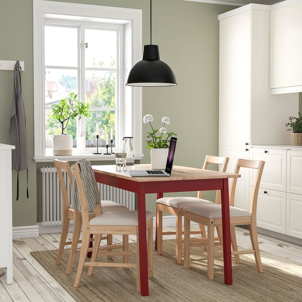 Red dining setup with cushions, warm light, laptop, plant. Bright kitchen space.