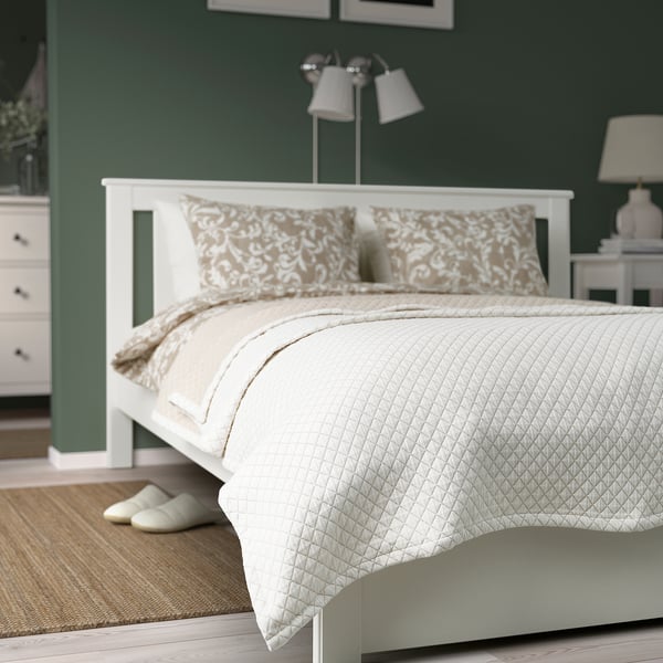 Prakvial bedspread in off-white, quilted, covering double bed, larger than slippers nearby, made of recycled polyester and cotton.