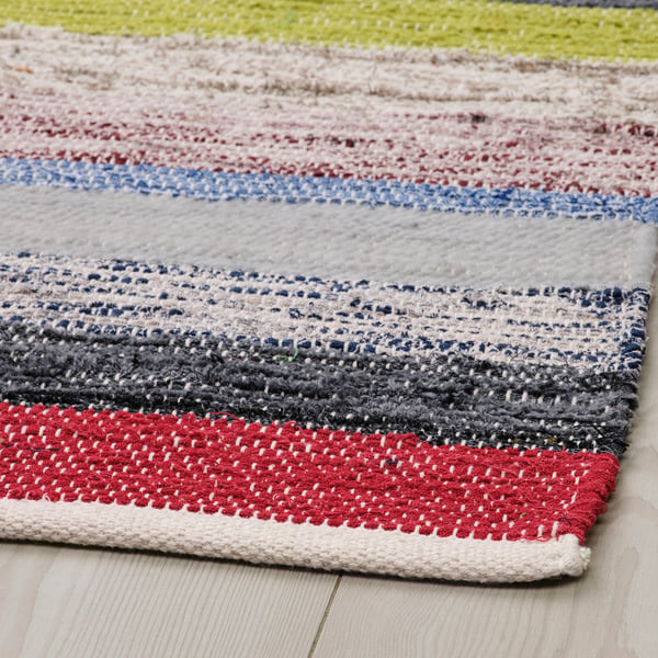 Colourful, handwoven cotton rug displayed on a wooden floor, showcasing a mix of vibrant and neutral stripes.