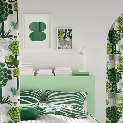 Bedroom with green bedding and wall art. RÖDALM picture frames above bed, smaller than walls.