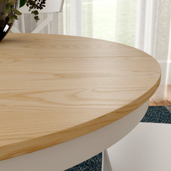 Round wooden table with light finish and white base, set in a bright room.