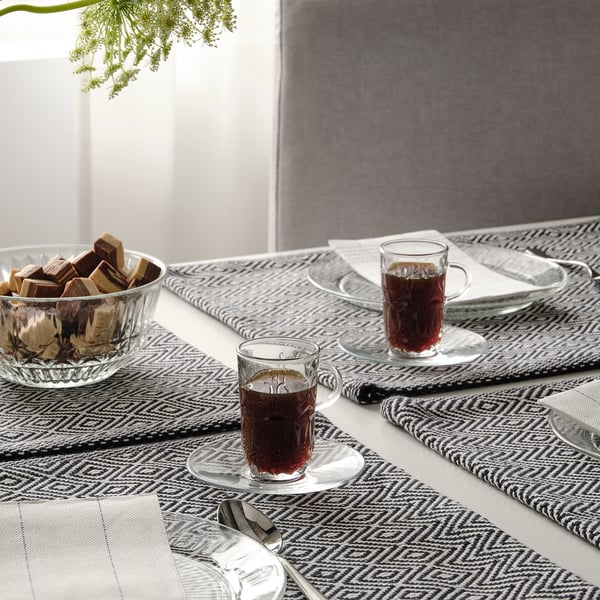 Table set with SÄLLSKAPLIG glasses, cups, and saucers; bowl of chocolates, napkins, and cutlery.
