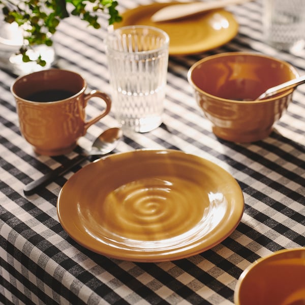 Ochre yellow ceramic plates & mugs on checked tablecloth. Small, rustic, handmade feel.