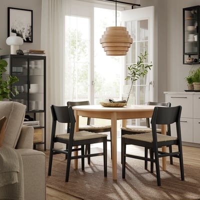 Modern dining area with SKANSNÄS light wood table surrounding by black chairs, unique pendant light, large window.