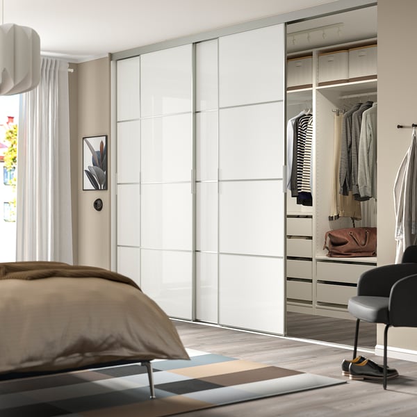Modern bedroom with large mirrored wardrobe, neatly arranged clothes, and soft lighting.