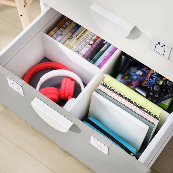 White SMÅSTAD storage drawers holding books, notebooks, and red headphones. Organised with dividers.
