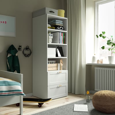 Grey and white SMÅSTAD bookcase with books, clothes, decor, a small bed, and framed art.