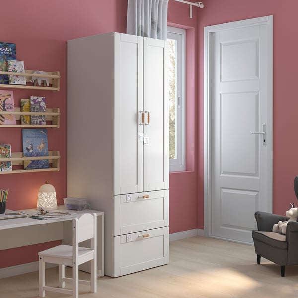 Childrens room with white SMÅSTAD wardrobe, shelves, desk, and chair. Pink walls, wooden floor, grey armchair, and stuffed animals.