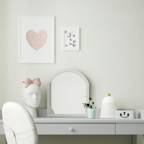 Minimalist desk setup with mirror, chair, makeup tools, and artwork.