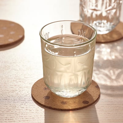 A glass filled with water on a round cork coaster on a wooden table.