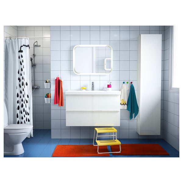 Modern bathroom with lighted mirror, yellow step stool, colourful towels, and playful curtains. Blue floor, white walls, blue towels hanging.