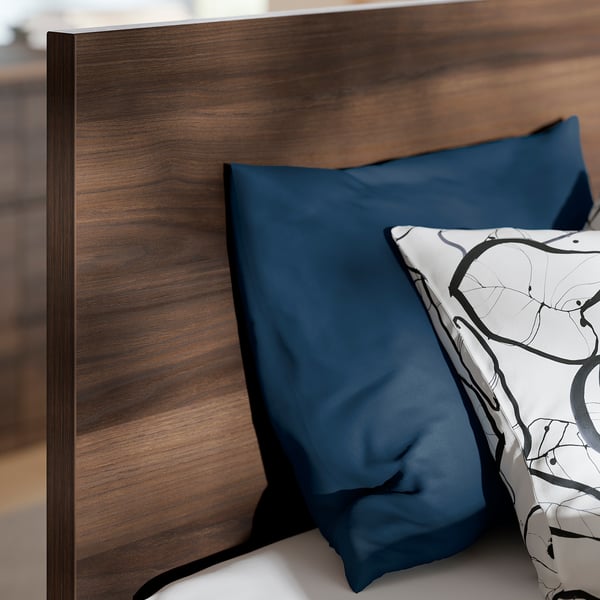 Close-up of wooden headboard with modern design, leaning against it blue pillow, one white with abstract pattern.
