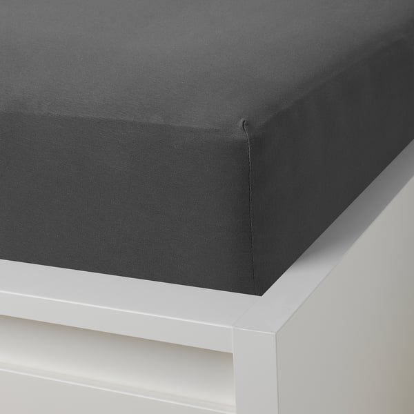 Dark grey fitted sheet with elastic edges on a white bed frame.