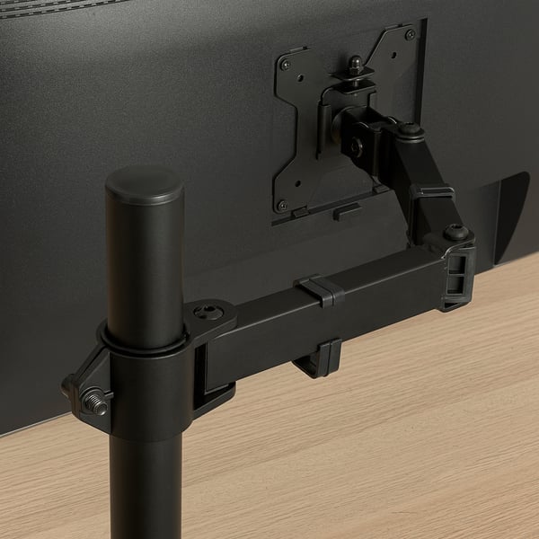 Black monitor arm bracket securely mounted on wooden desk, showing sturdy metal construction and adjustable angles for optimal screen positioning.