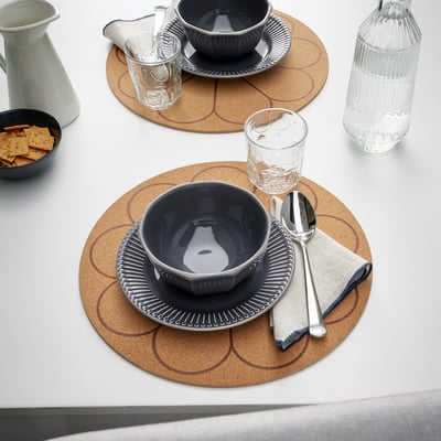 Table setting with grey plates, bowls, and glasses on round cork mats.