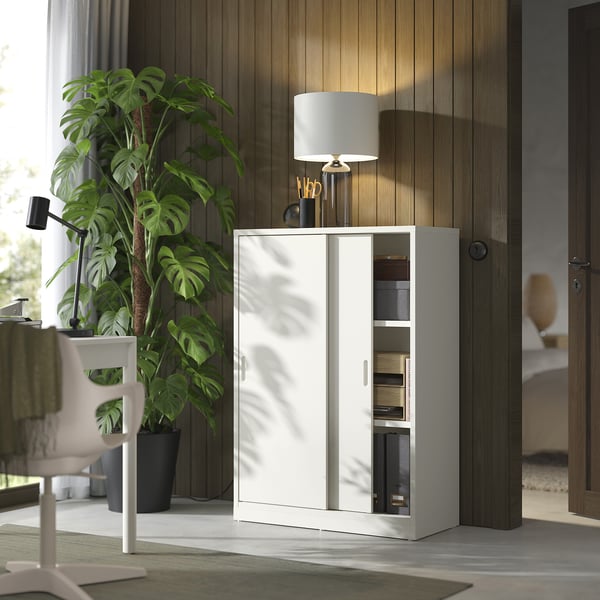 Modern home office scene with white TONSTAD storage cabinet, sliding doors, green plant, and desk.