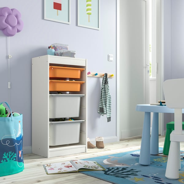 Childs room with white TROFAST storage unit, orange and grey bins, books, and blue table.