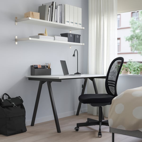Home office setup: small black TROTTEN desk with laptop, chair, shelves, and window.