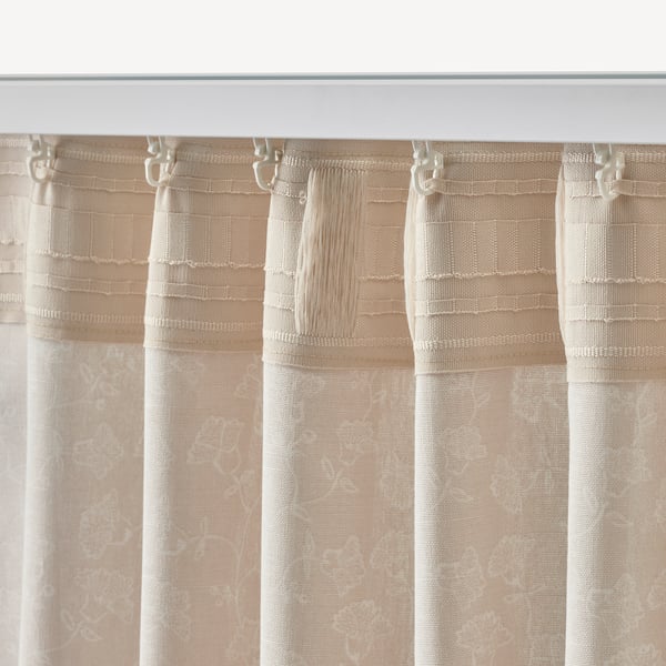 Sheer beige curtains with white floral patterns hang from hooks, filtering light and offering privacy. Soft, decorative fabric.