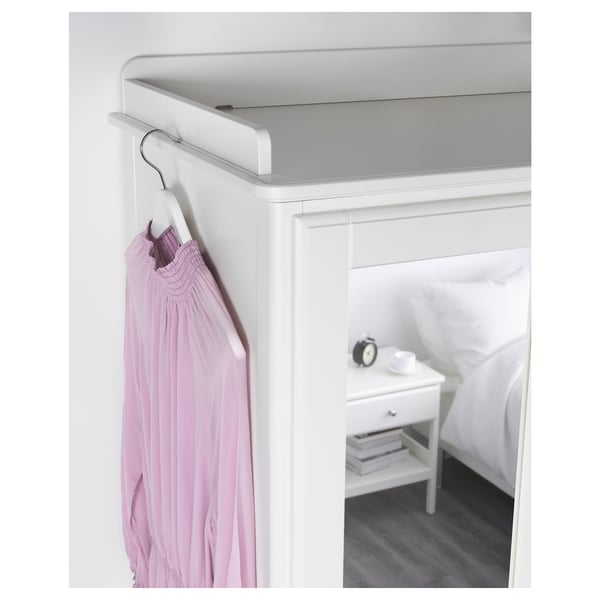 A modern white wardrobe with a groove for hanging clothes, a drawer, and adjustable feet.