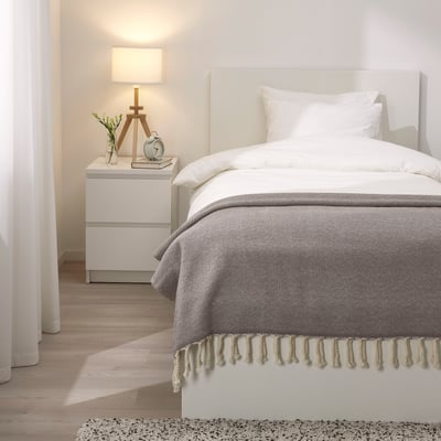 Elegant bedroom with grey wool throw blanket, white bed, and bedside table with lamp.