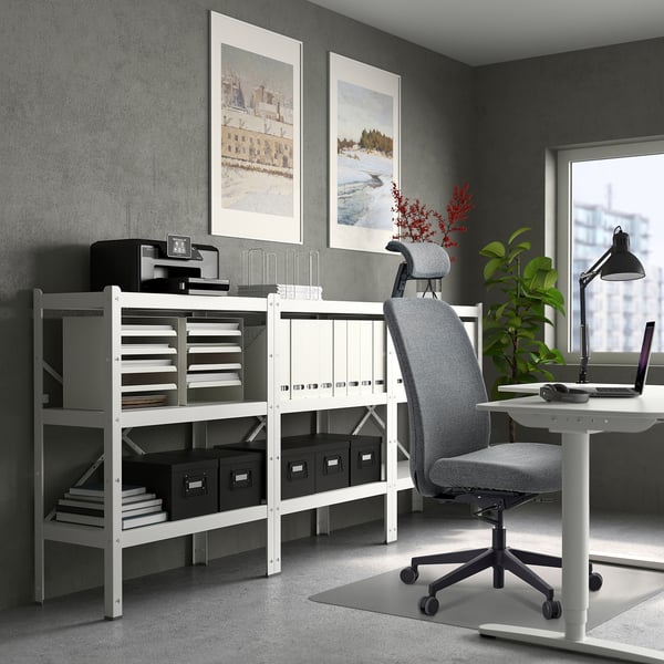 A modern home office setup with a white VALLFJÄLLET office chair, a white desk, and well-organized shelves against a grey wall.