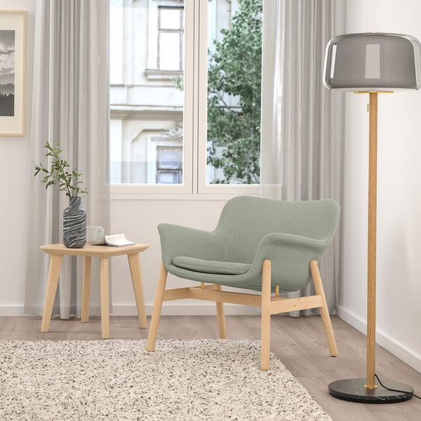 Minimalist living room with light grey VEDBO armchair, wooden side table, tall lamp, and large window.