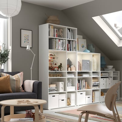 Modern home office with grey sofa, white bookshelves, wooden chair, and colourful rug.