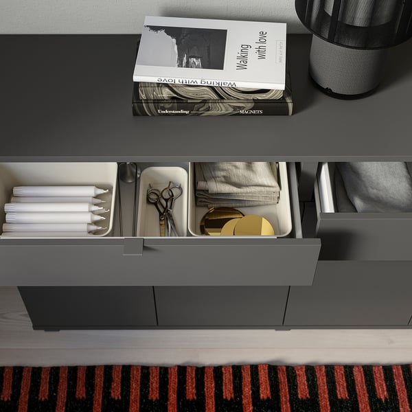 Modern grey sideboard with drawers and shelves organised with books, candles, scissors, and cloth.