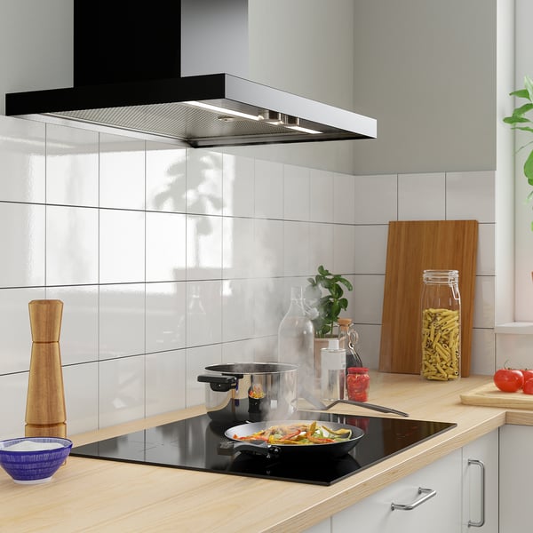 Modern kitchen with induction stove, colourful veggies, wooden counter & grey backsplash.