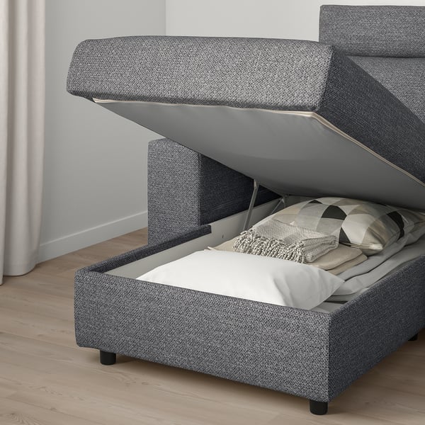 A grey fabric sofa bed with storage compartment open, revealing folded blankets and pillows.
