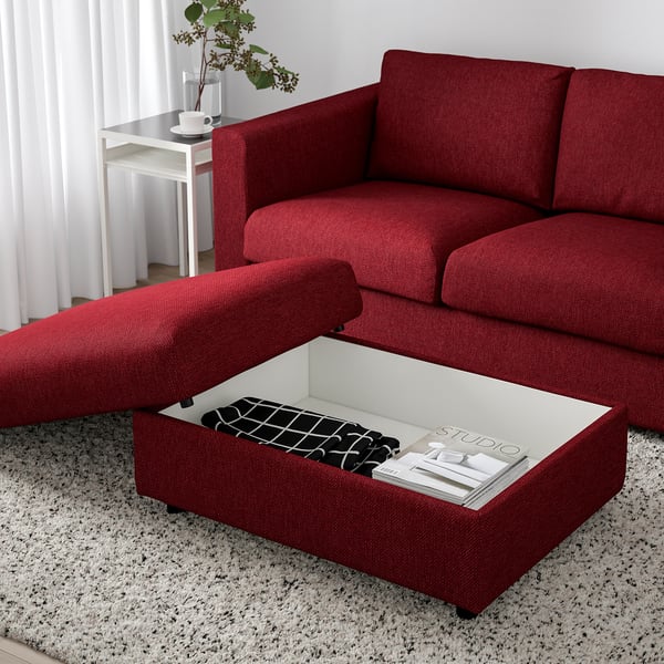 Red sofa with ottoman, lift-up seat revealing storage. On rug, near side table and plant.