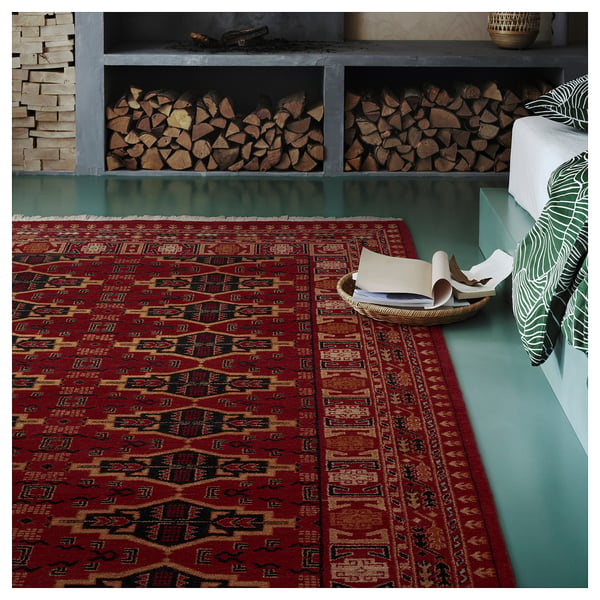 Burgundy geometric rug on teal floor, beside stacked logs and cushions.