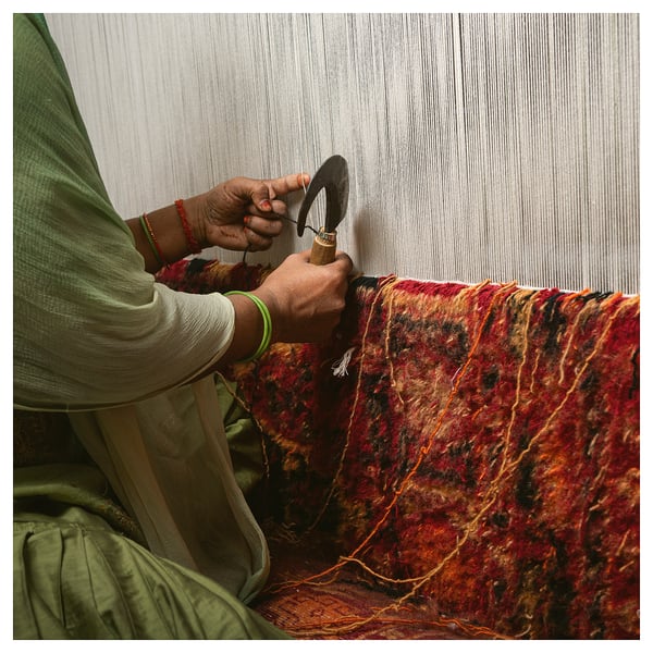 Person weaving colourful, handmade rug.