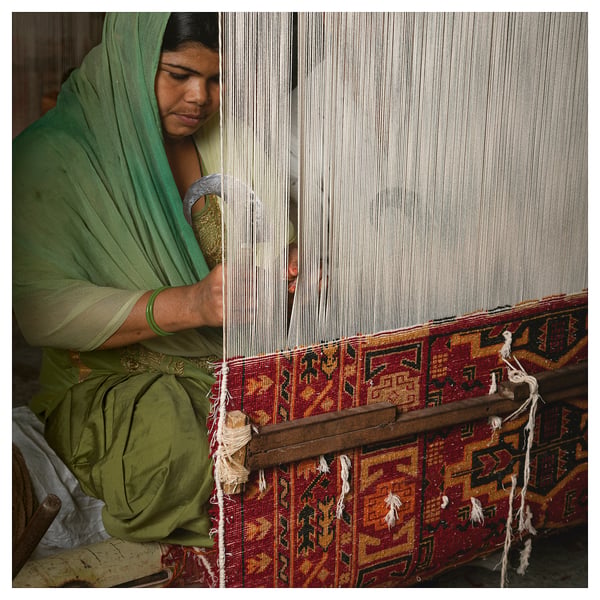 Person weaving colourful rug. Green attire, intricate patterns.